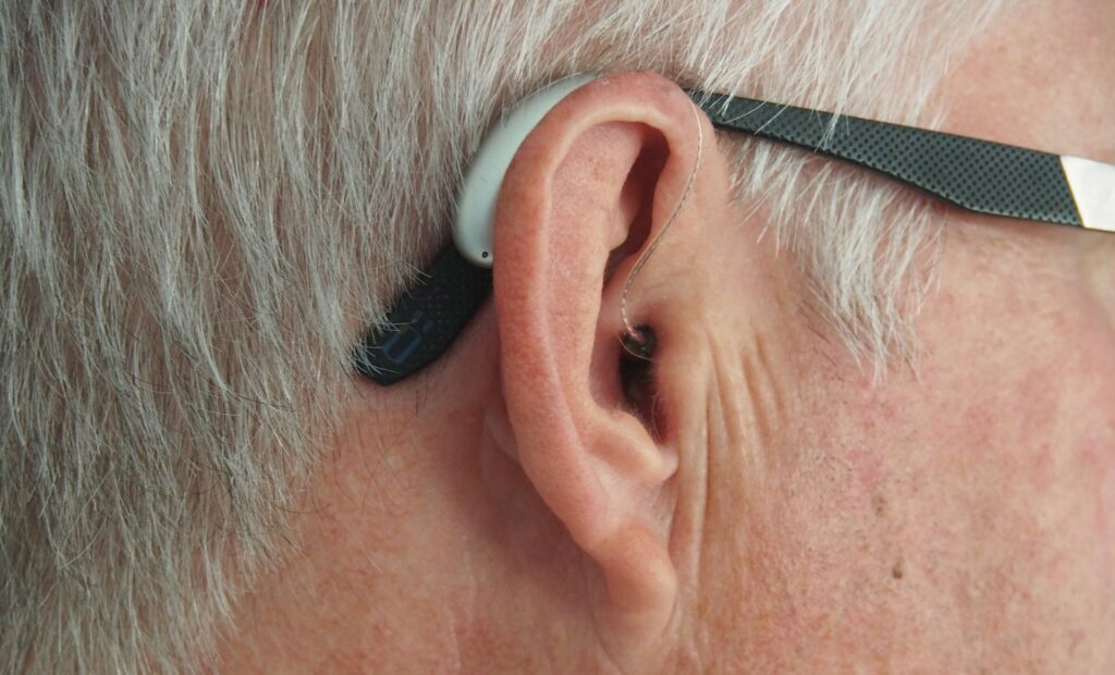 Close up of man with grey hair wearing glasses and with a hearing aid